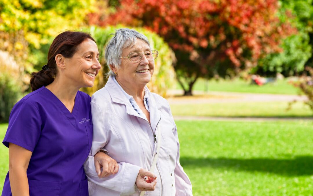 Caregiver walking arm in arm with a senior woman in a park in fall
