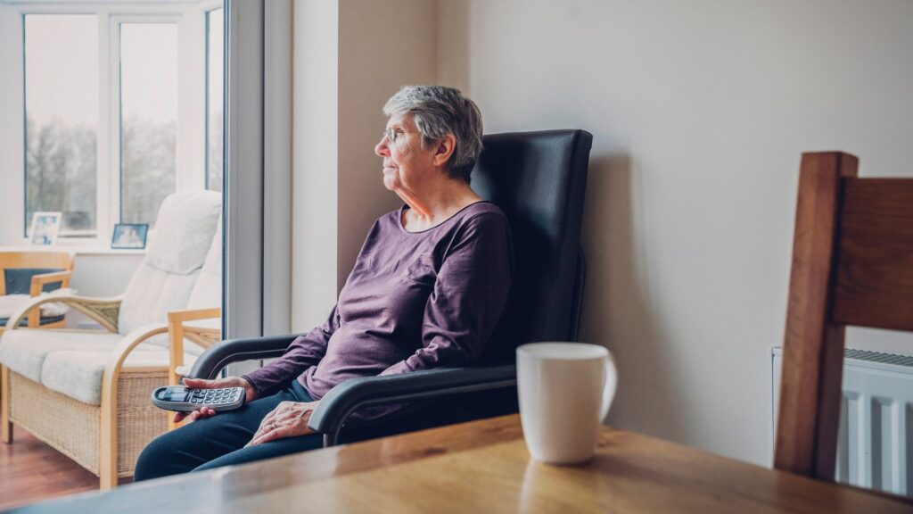 Senior woman sitting by a window at home holding a phone